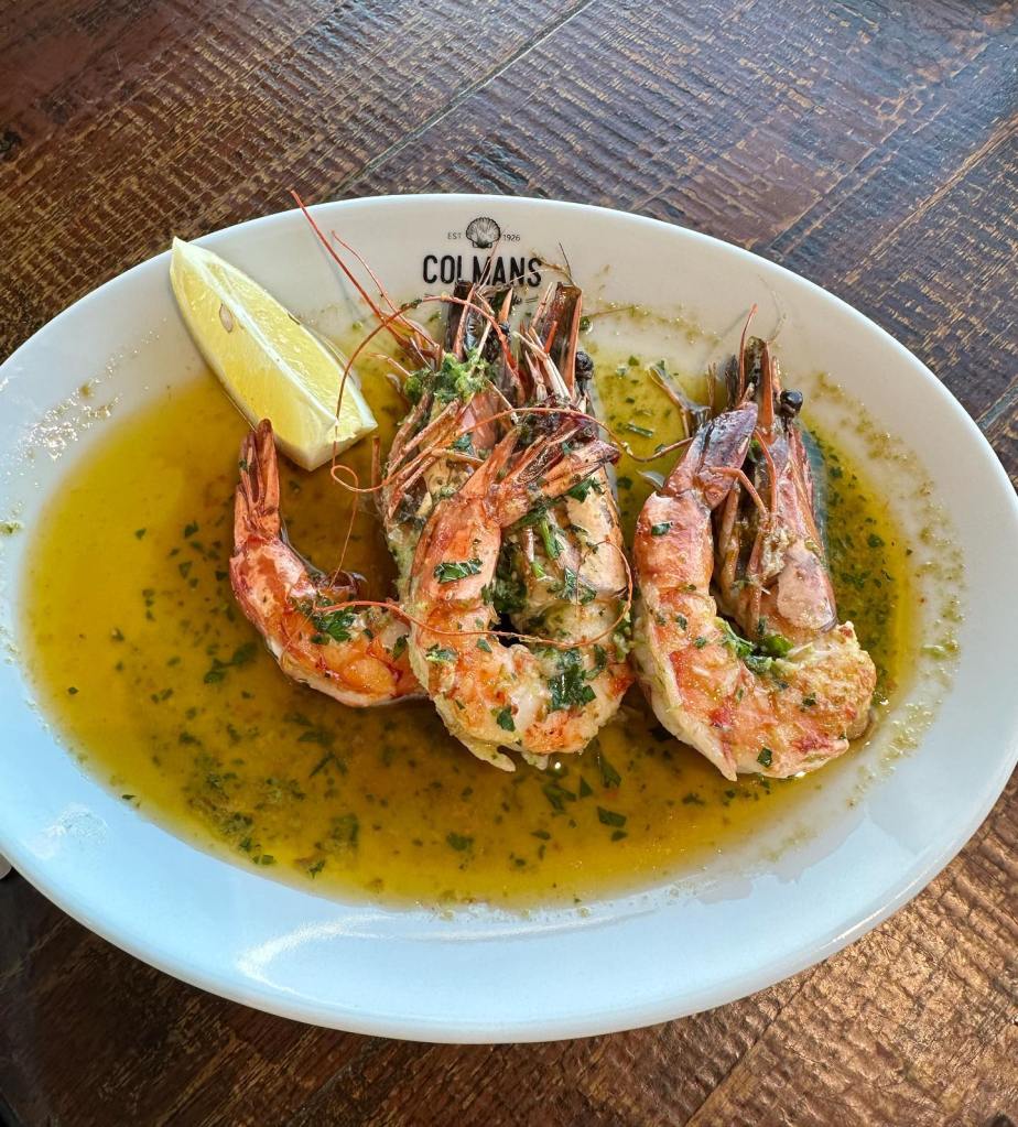 Fresh prawns served on a plate with garlic butter and herbs, served with a wedge of lemon