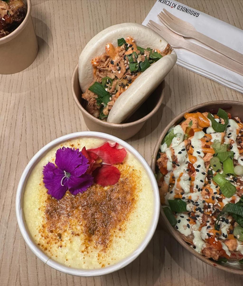 Turmeric latte with a flower garnish, Gochujang salmon bao bun and a prawn udon noodle bowl. A table of colorful food perfectly presented with flowers.