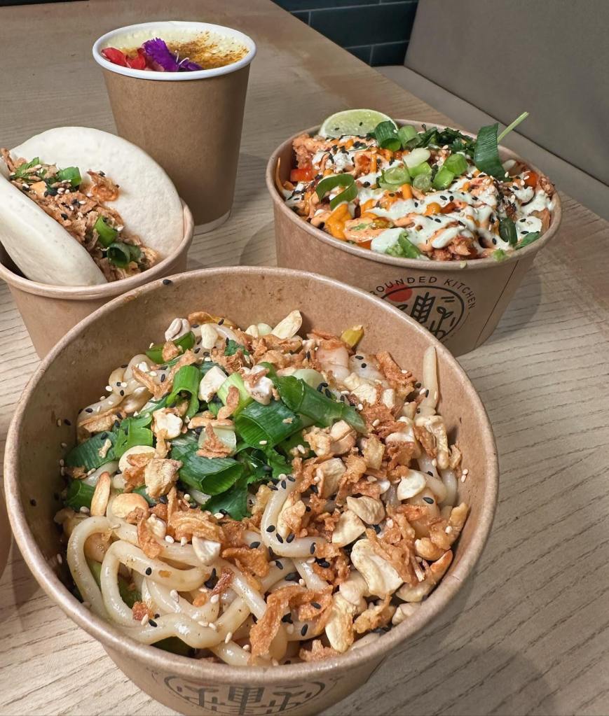 Turmeric latte with a flower garnish, Gochujang salmon bao bun and a prawn udon noodle bowl Korean wings and a salmon rice bowl. A table of colorful food perfectly presented with flowers at the grounded kitchen metrocentre gateshead