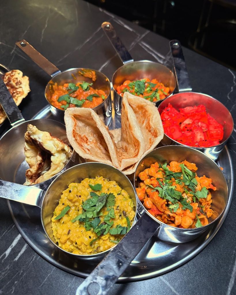 Indian Thali Tray Nastha featuring bhuna, channa, dhal, masala beans, parathas, spiced potatoes, and egg omelette, served with masala chai.