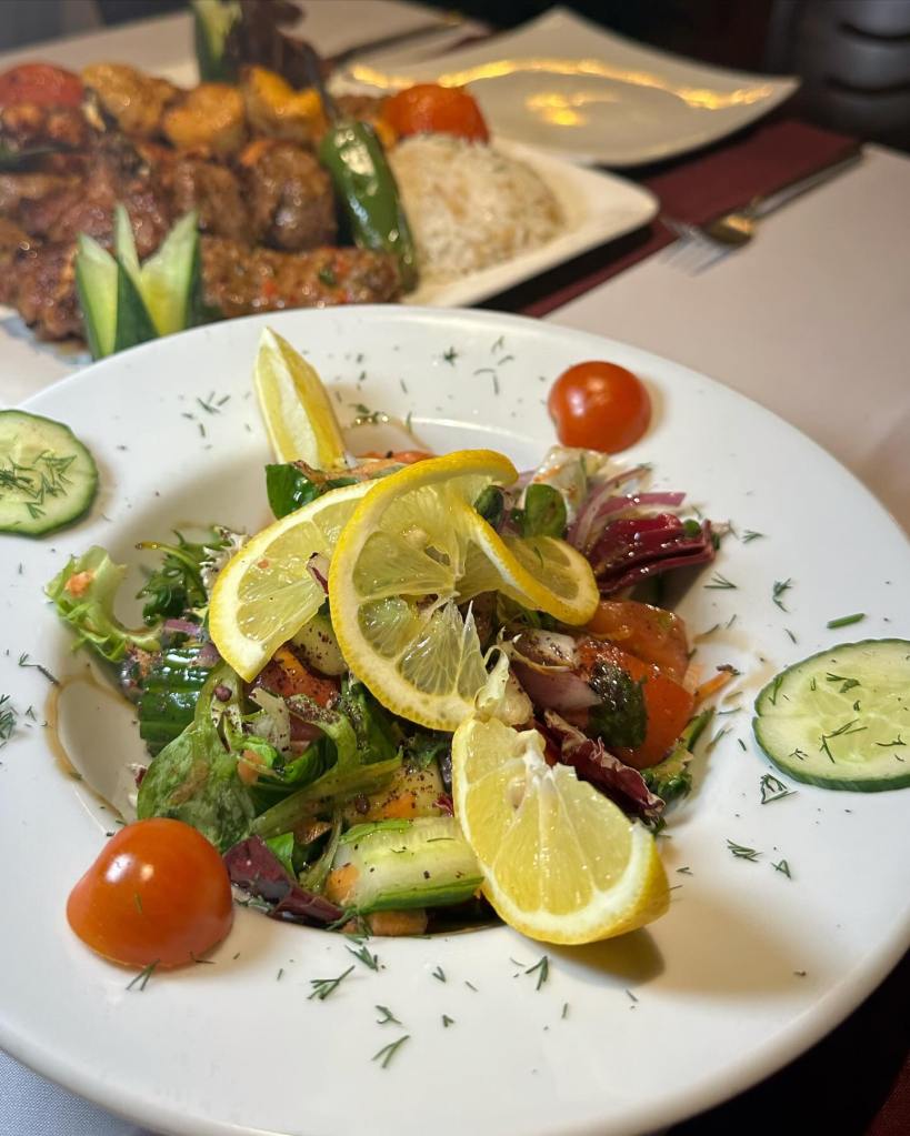 A colorful side salad garnished with sliced lemon chopped tomato and cucumber and a sprinkle of dill.