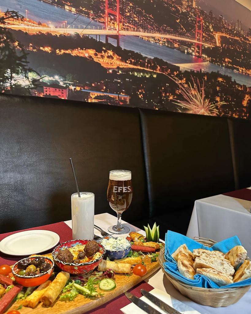 A vibrant cold sharing platter featuring homemade hummus, tzatziki, olives, and freshly baked bread, beautifully arranged on a wooden board, pared with freshly cooked breads and a glass of ayran