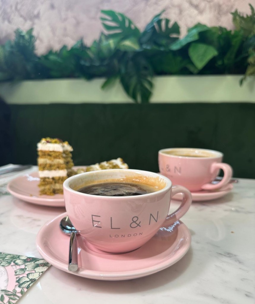 Café Interior: A stylish café space with light colors, modern lighting, neon signs, and lush greenery and powder pink coffee cups