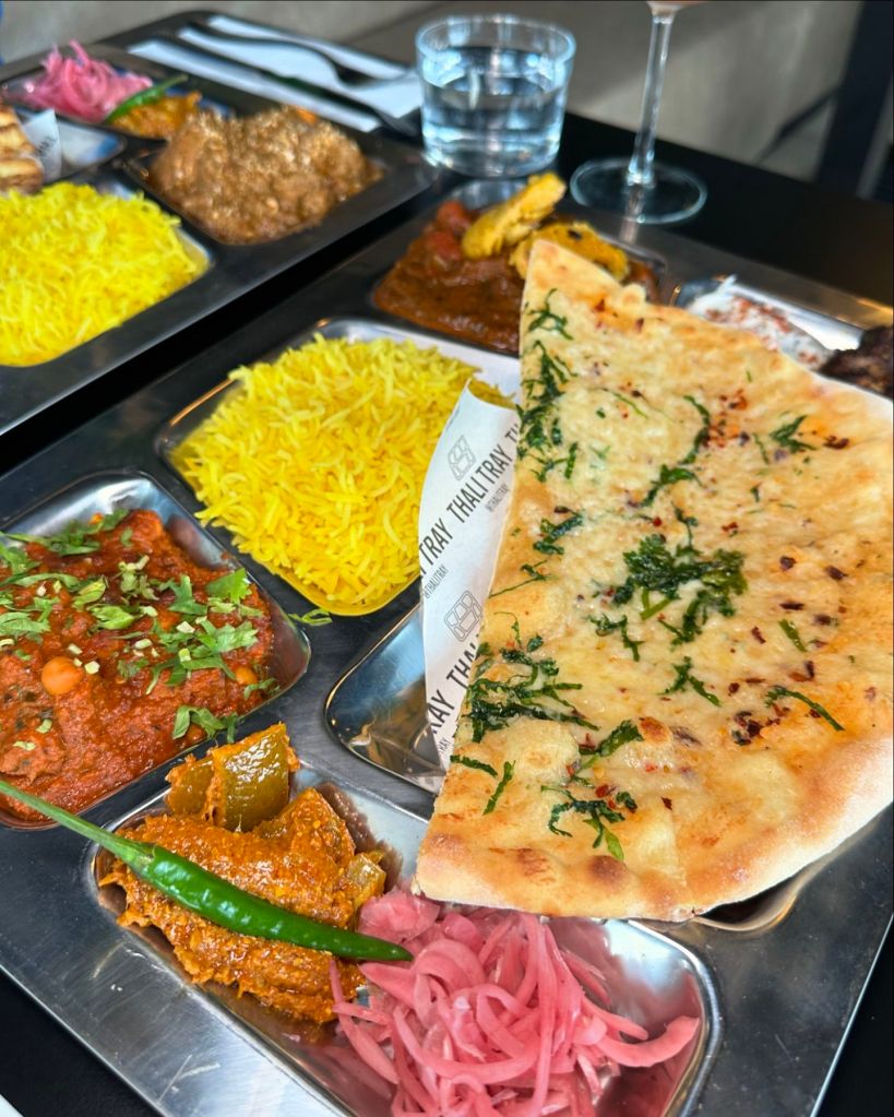 Vegetarian Punjabi Thali from Thali Tray, featuring Chickpea Chole, Spinach & Mushroom Palak, and Cheese Garlic Naan. Also Goan Thali from Thali Tray, including Pork Belly Vindaloo, Chicken Xacuti, and accompanying sides