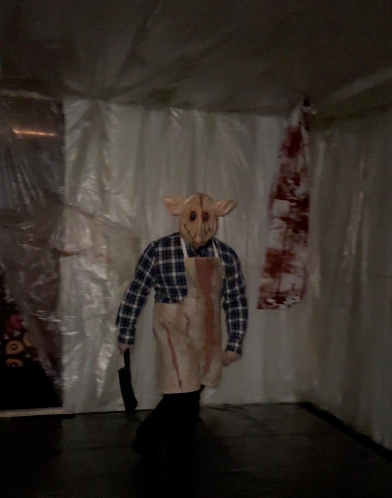 Nightmare at Rainton, a man in a pig mask and meat cleaver and blood on his apron. a scary Halloween walk scene