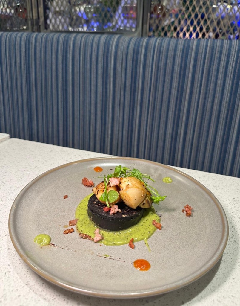 Scallops with Black Pudding: Rich and savory scallops with black pudding and pancetta on minted spring onion pea purée, served as a starter at Mamas Bar and Grill