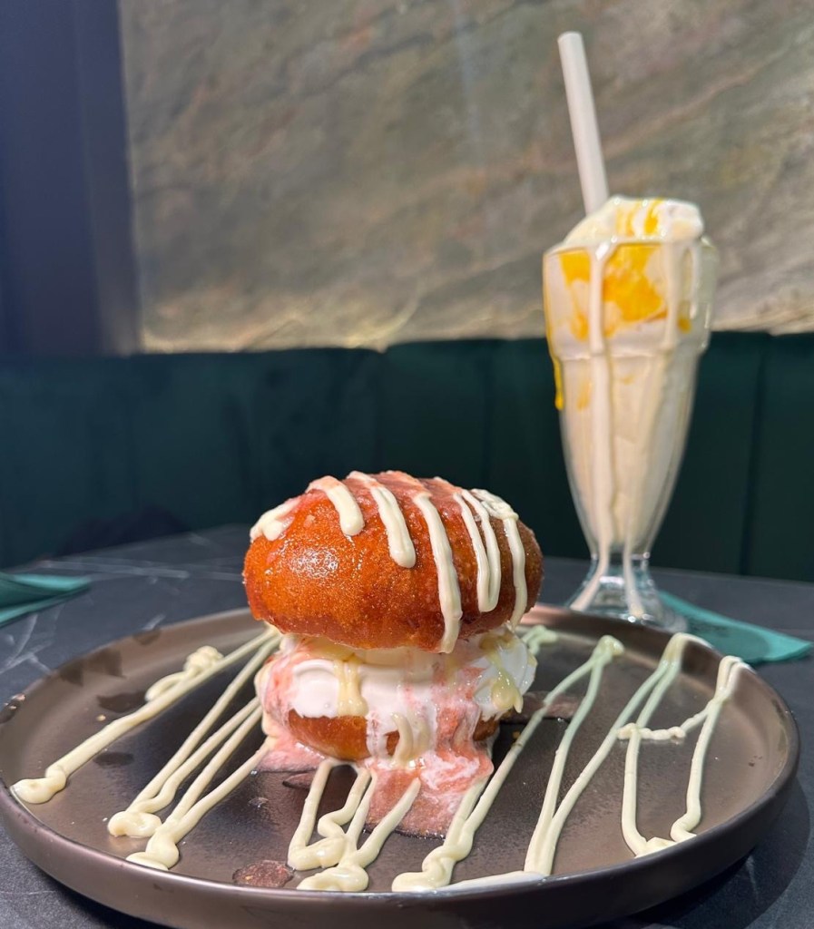An IceBurg, A fried and sugar-coated brioche bun sliced in half, with a scoop of creamy vanilla ice cream sandwiched inside with red strawberry and sauce, creating a unique and decadent dessert