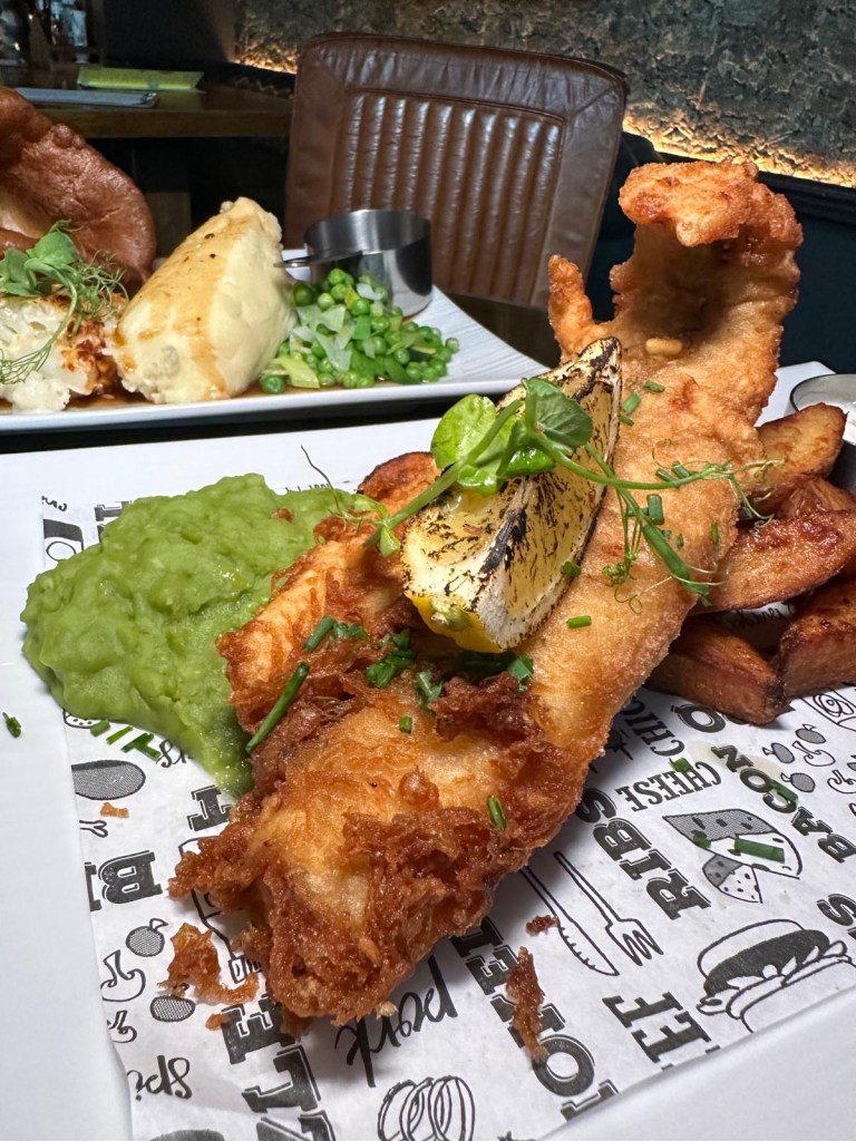 Fish & Chips, Crispy haddock fried in brown ale batter, served with homemade chips, vibrant mushy peas, and a tangy tartar sauce.