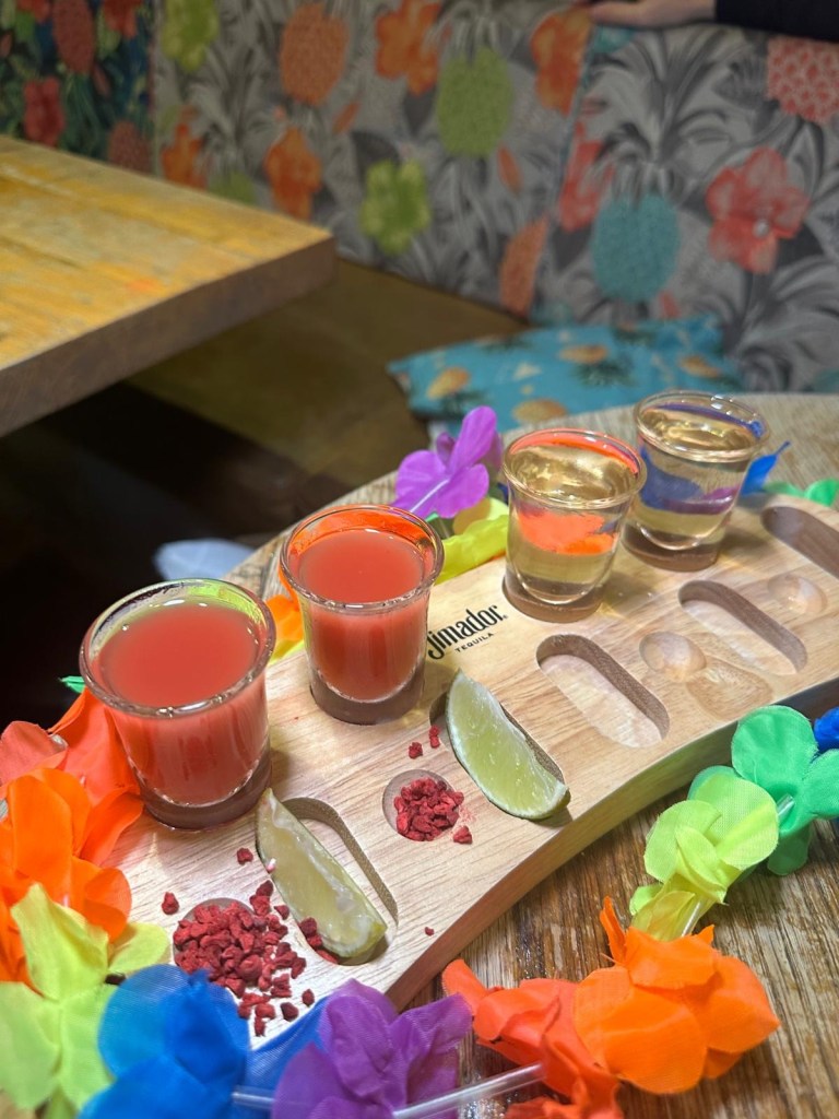 A colorful selection of festive cocktails from Revolution de Cuba, including a Merry Cherry Cuba Libre, Strawberry Margarita, and a shot tray with spicy mango and raspberry garnishes