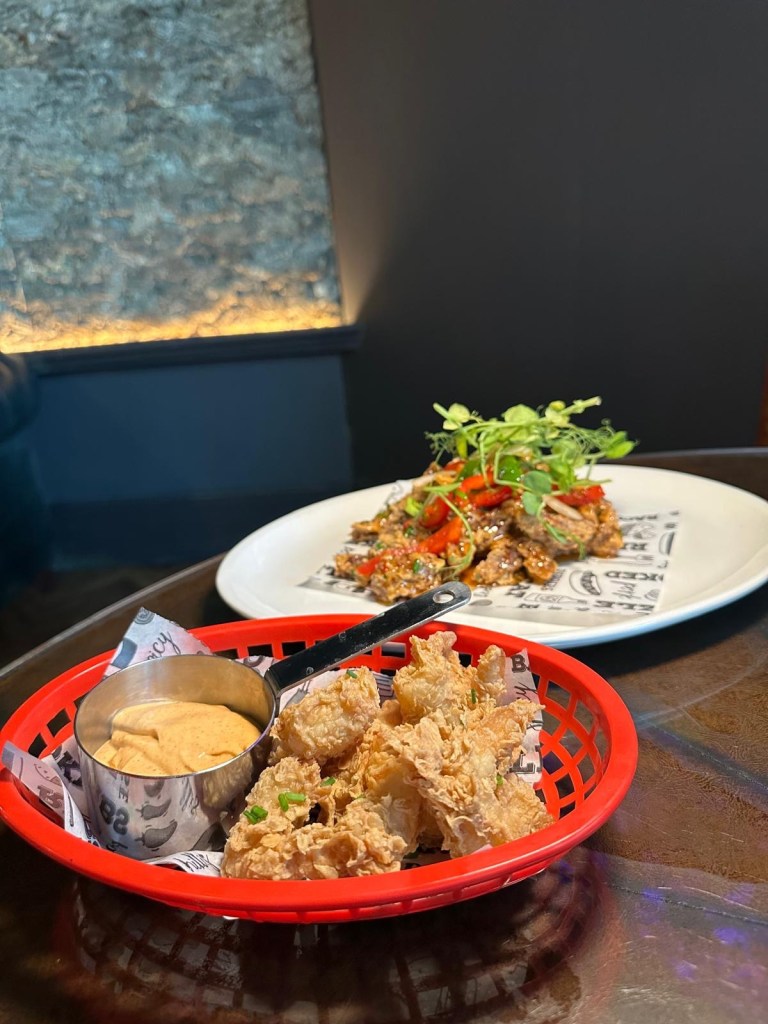 Crispy Beef, A plate of crispy, shredded beef coated in a glossy sweet chili sauce, served as a savory and tangy starter and Tiger Prawns, Golden beer-battered tiger prawns presented with a side of zesty Bloody Mary dipping sauce.
