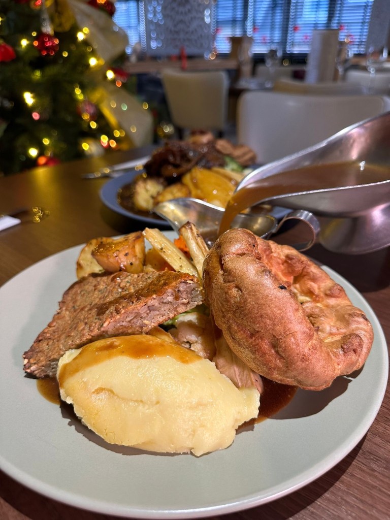 Vegetarian nut roast served with Yorkshire pudding, crispy roast potatoes, creamy mash, seasonal vegetables, and a drizzle of rich gravy