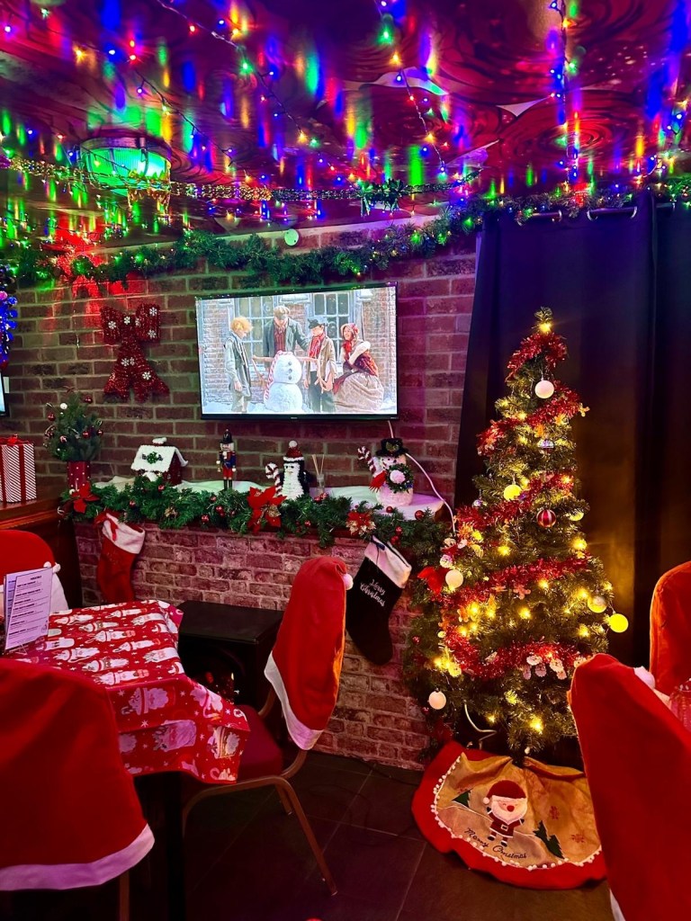 A cozy festive fireplace adorned with tinsel, retro decorations, and multicolored lights at Rusty’s Christmas pop-up bar. An immersive Christmas wonderland with 80s-inspired decor, classic festive films playing in the background, and sparkling tinsel hanging from every corner.