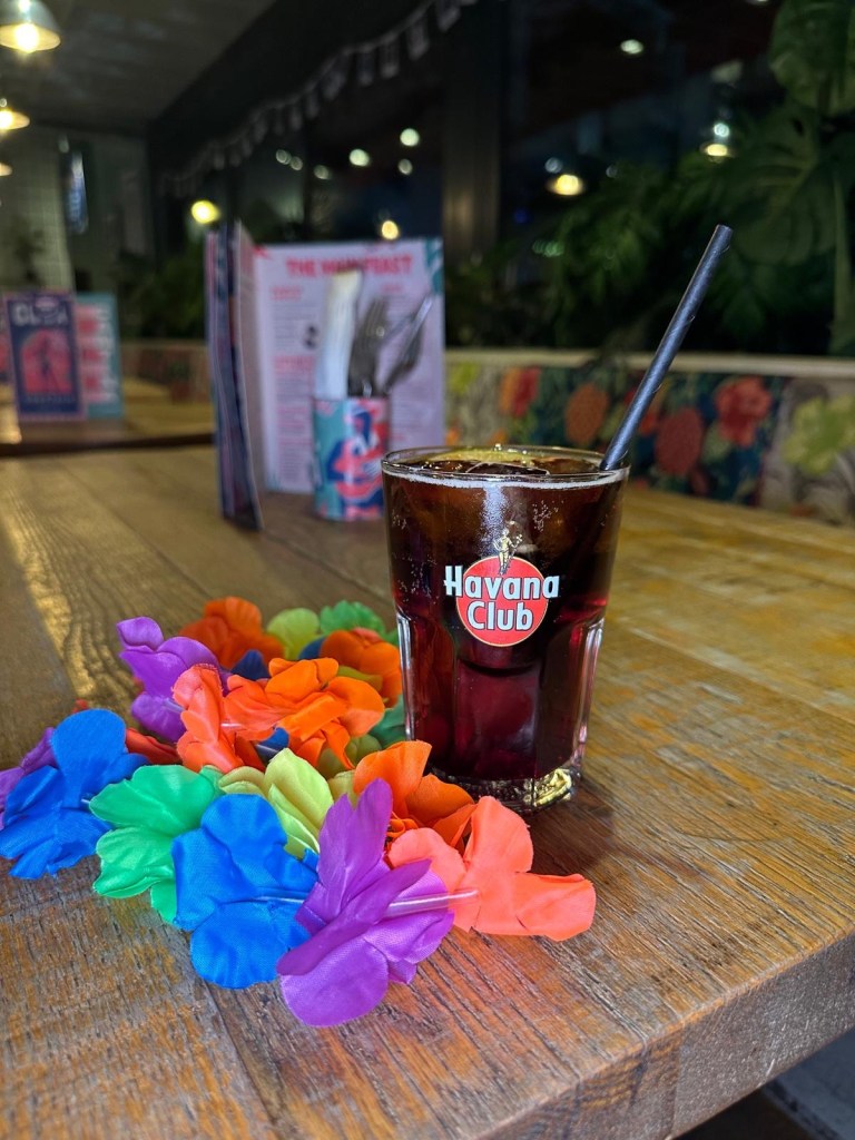 A colorful selection of festive cocktails from Revolution de Cuba, including a Merry Cherry Cuba Libre, Strawberry Margarita, and a shot tray with spicy mango and raspberry garnishes