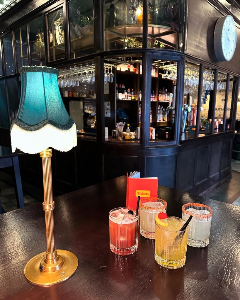 A selection of cocktails from Tickets bar, including a watermelon mojito, spicy margarita, Festive Royale, and raspberry martini, displayed on a wooden table