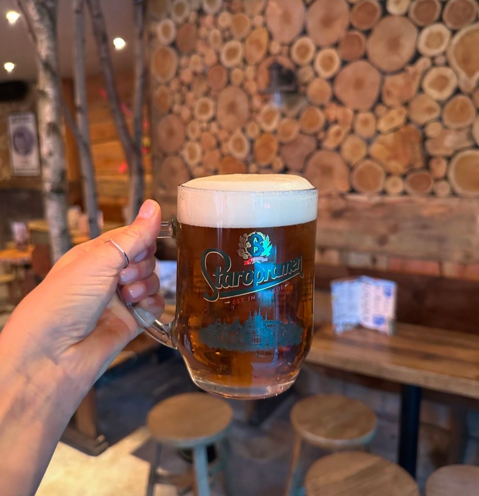 An authentic pint of Staropramen beer, held up in a ski bar with rough sawn wood cladding.