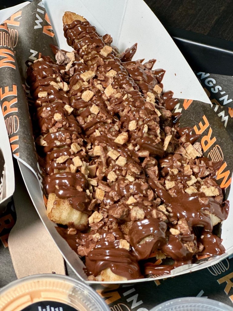 Churros: A portion of churros, crisp and golden on the outside, soft on the inside, topped with pistachio chocolate and drizzled with milk chocolate.