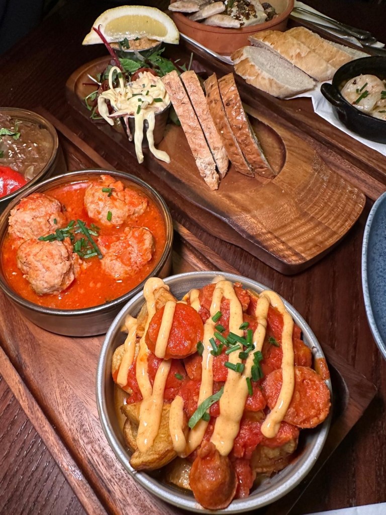 Classic Patatas Bravas: Crispy Patatas Bravas topped with chunks of spicy chorizo, a drizzle of aioli, and a rich bravas sauce, served in a tapas-style dish. Also Pork and Chorizo Meatballs: Close-up of juicy Pork and Chorizo Meatballs, packed with flavor and served in a delicious tomato-based sauce