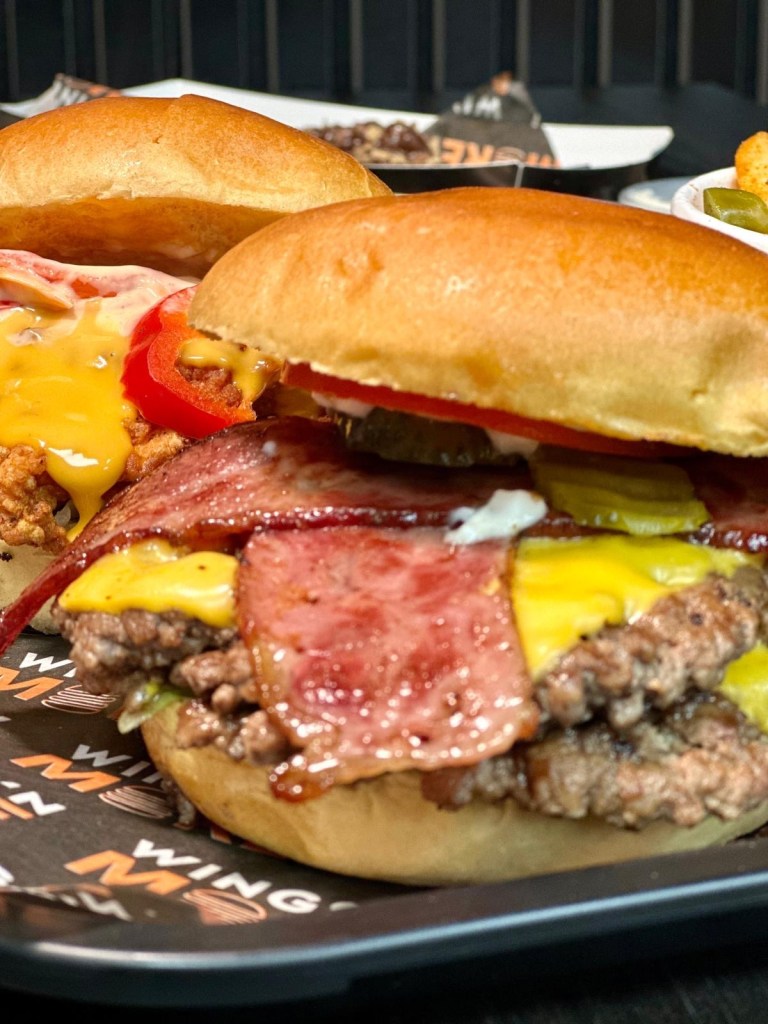 A stacked smash burger with a seared patty, crispy bacon, melted cheese, and drizzled with signature sauce, served in a soft brioche bun.