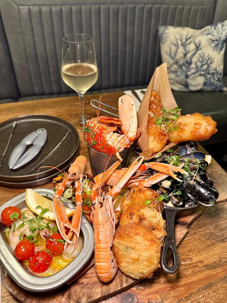 Angler Board at Dodgin’s Yard featuring garlic butter lobster, Stella Maris langoustines, fish cakes, cod goujons, moules marinière, garlic prawns, and firecracker salmon, beautifully plated on a rustic wooden board, showcasing fresh, locally sourced seafood