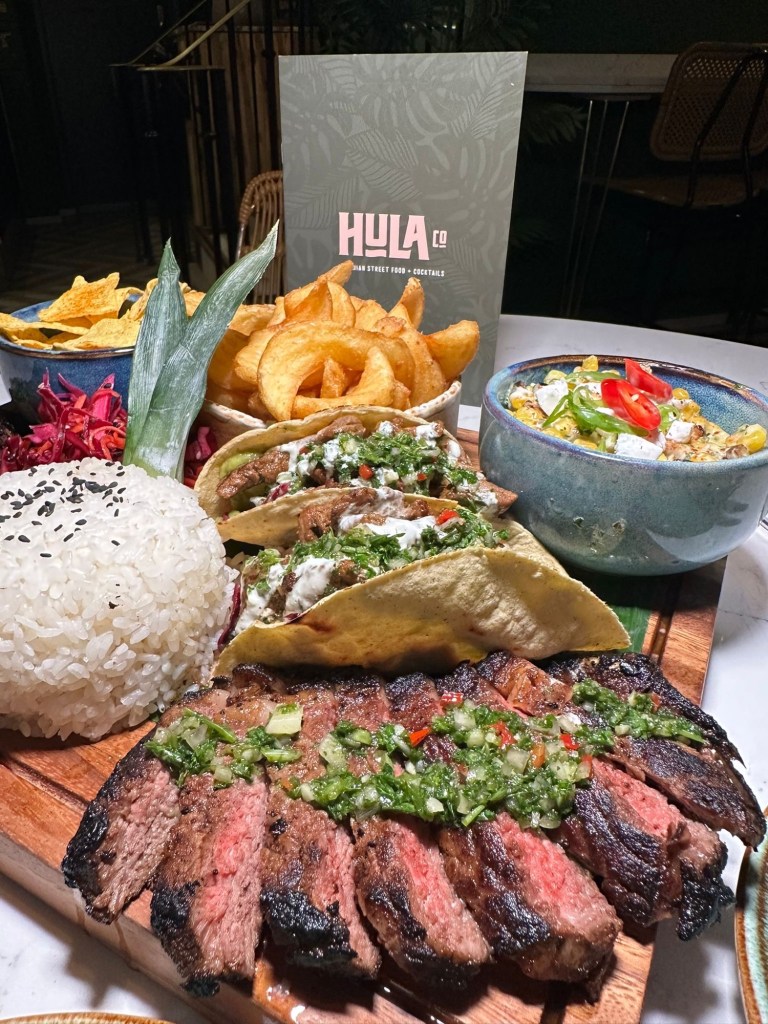 Steak Sharing Board: Tender birria strip loin steaks with steak tacos, chimichurri, pickled slaw, sticky rice, corn luu, and crispy potato sidewinders