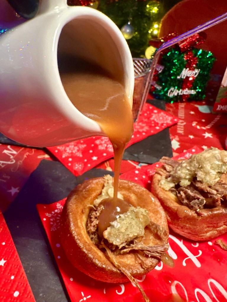 Three festive nibbles: crispy Mini Yorkshire Puddings filled with slow-roasted beef, stuffing, and gravy, served on a rustic plate. Golden Baked Camembert Rounds, crispy on the outside and gooey inside, paired with a festive garnish. A plate of crispy Cauliflower Wings drizzled with vegan sriracha mayonnaise, served as a vibrant festive snack.