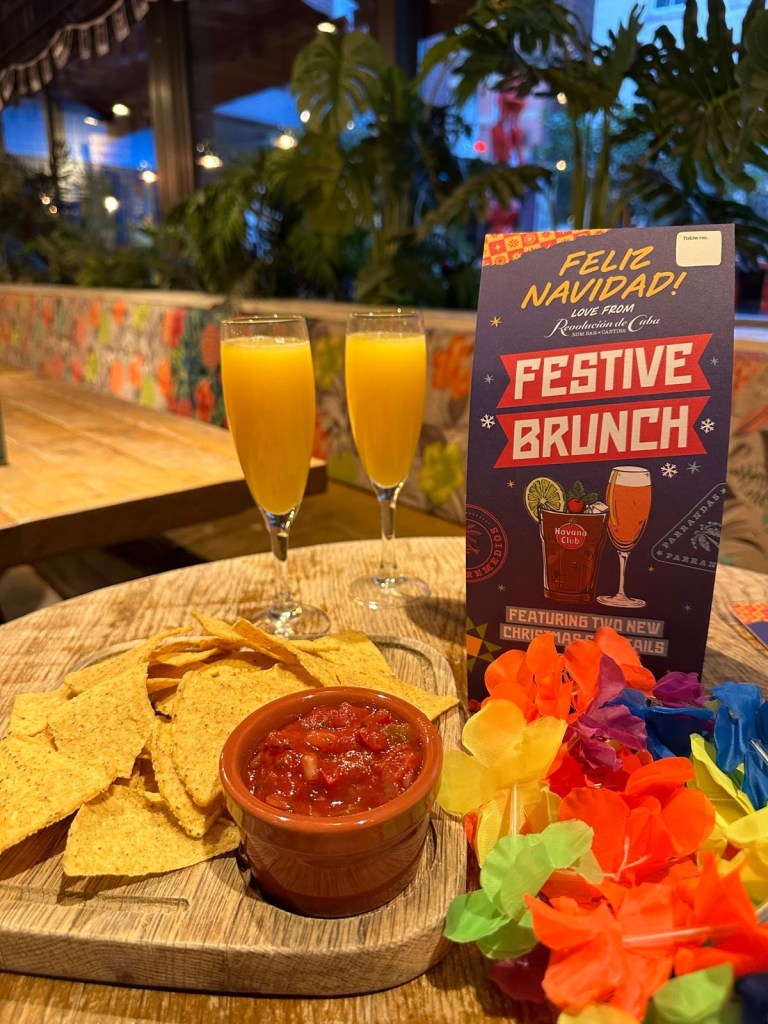A colorful selection of festive cocktails from Revolution de Cuba, including a Merry Cherry Cuba Libre, Strawberry Margarita, and a shot tray with spicy mango and raspberry garnishes
