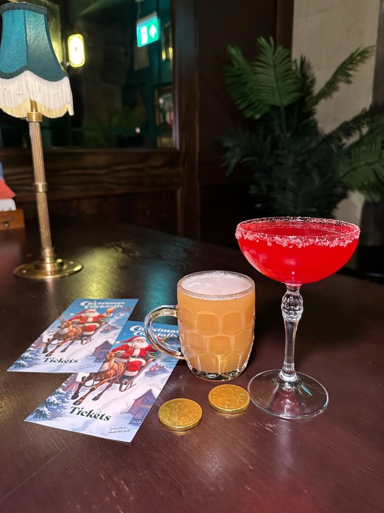 Butter Beer cocktail at Tickets bar, served in a glass mug with a frothy top. Sat on a table with christmas candy and Christmas menu