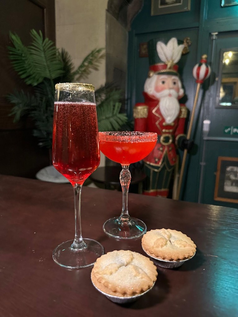 Festive Christmas cocktails at Tickets bar in Newcastle, featuring a glittering Festive Royale and sherbet-rimmed Tinseltini. In the background is a giant nutcracker and 2 sweet mince pies on the table.