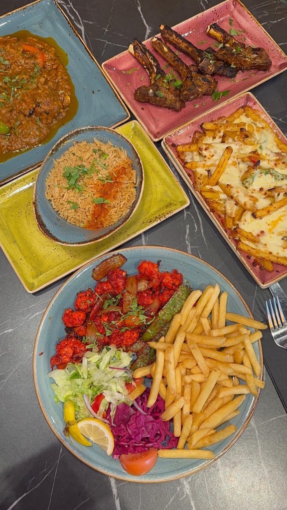 A tempting spread of Grill n Chill's signature dishes displayed on a booth table, showcasing their diverse menu. From rich curries and perfectly grilled lamb chops to indulgent cheesy chips and fresh salads, the variety highlights the restaurant's hearty and flavorful offerings