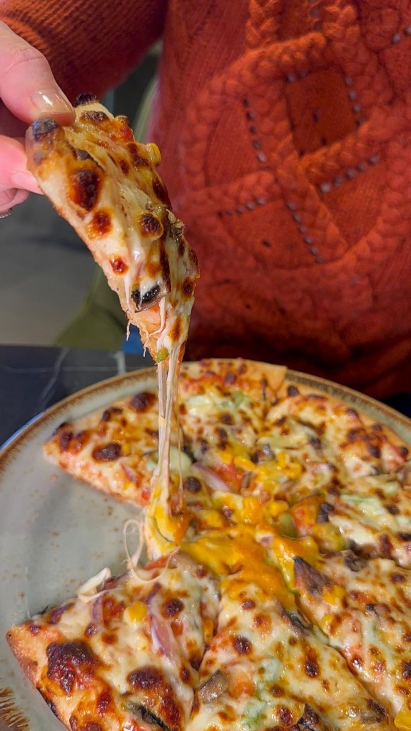 A freshly baked vegetarian pizza loaded with colorful vegetable toppings, melted cheese, and a side of garlic mayo