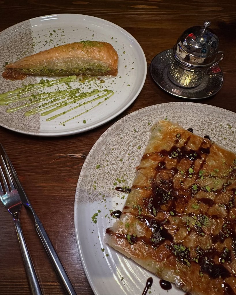Plate featuring two Turkish desserts: crispy triangle baklava layered with pistachios and sweet syrup, alongside delicate Katmer pastry filled with pistachios and milk skin at Saray Turkish Restaurant, Jesmond