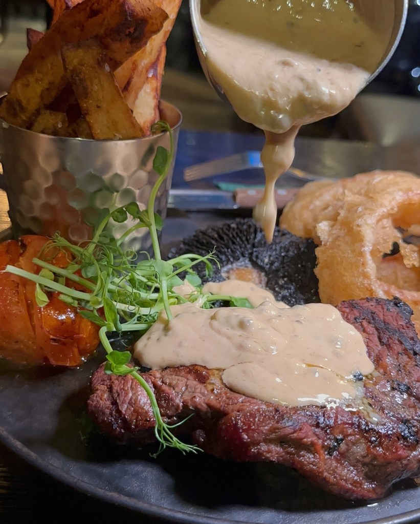 8oz sirloin steak at Sticky Wicket, served with hand-cut chips, chargrilled tomato, mushroom, crispy onion rings, and peppercorn sauce