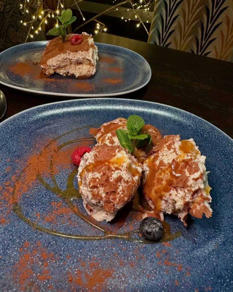 A decadent serving of homemade tiramisu with layers of coffee-soaked biscuits and cream alongside rich, white chocolate profiteroles at Fabio’s Italian Restaurant.