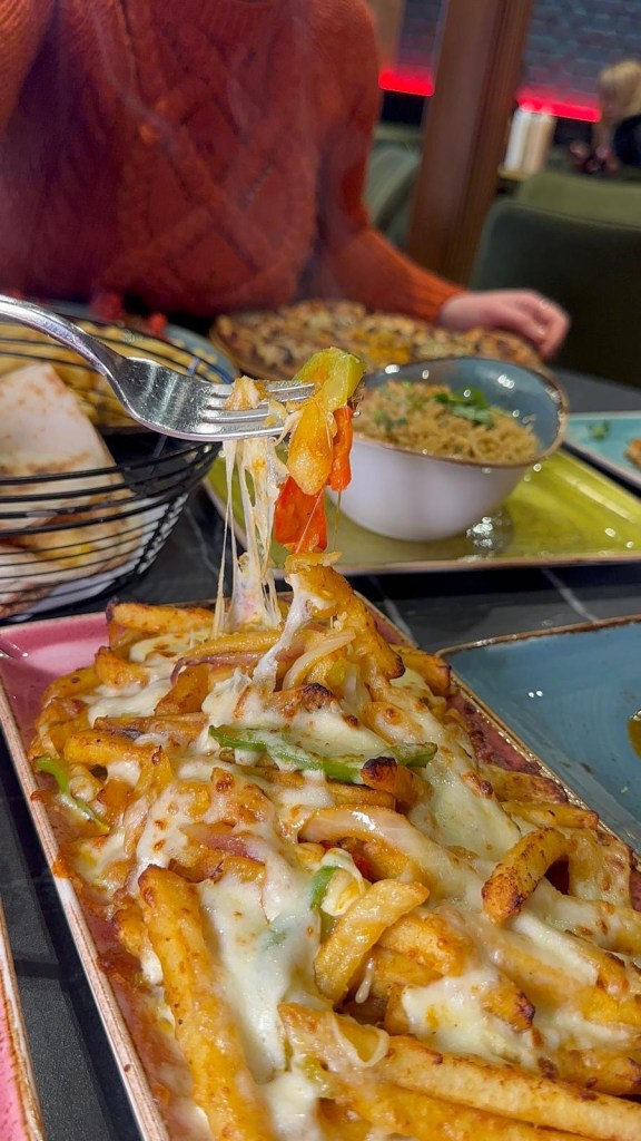 A plate of cheesy chips topped with vegetables, with melted cheese creating a satisfying cheese pull