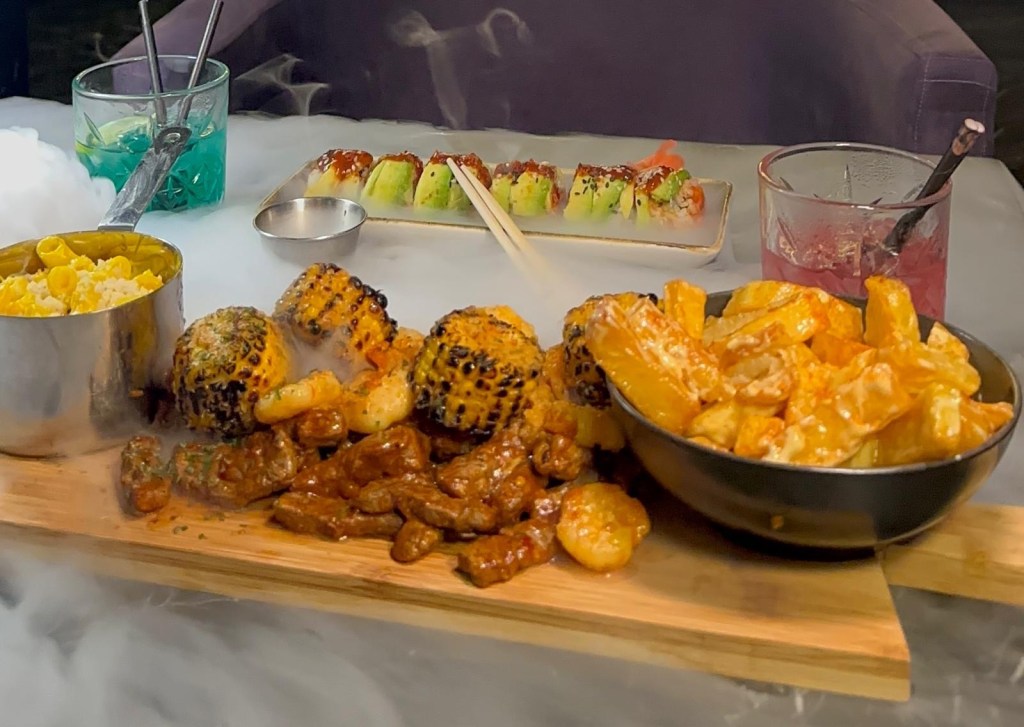 Surf and turf dish featuring grilled prawns, tender steak, seasoned chips, mac n cheese, and charred sweetcorn.