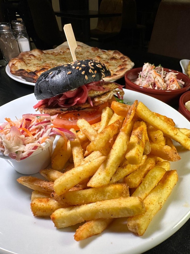 A Blackened Cajun Burger served in a charcoal bun with lettuce, tomato, pickled red onion, spiced mayo, and a side of house fries
