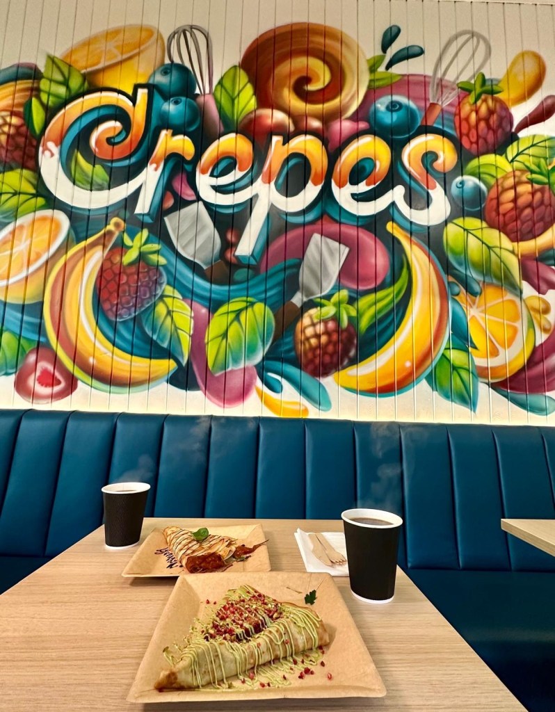 A table showcasing Crepes Gourmet's sweet and savoury crepes, topped with fresh ingredients, alongside a cup of coffee, set in a stylish cafe environment.