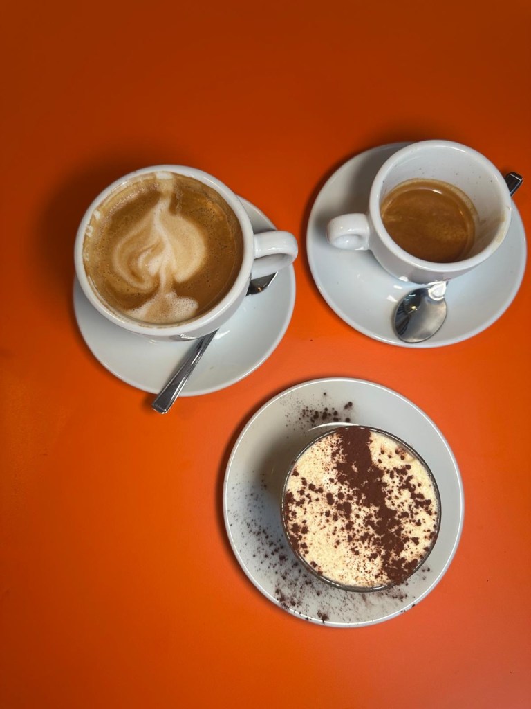 Rudy's Tiramisu served with an espresso and an oat milk latte on a wooden table
