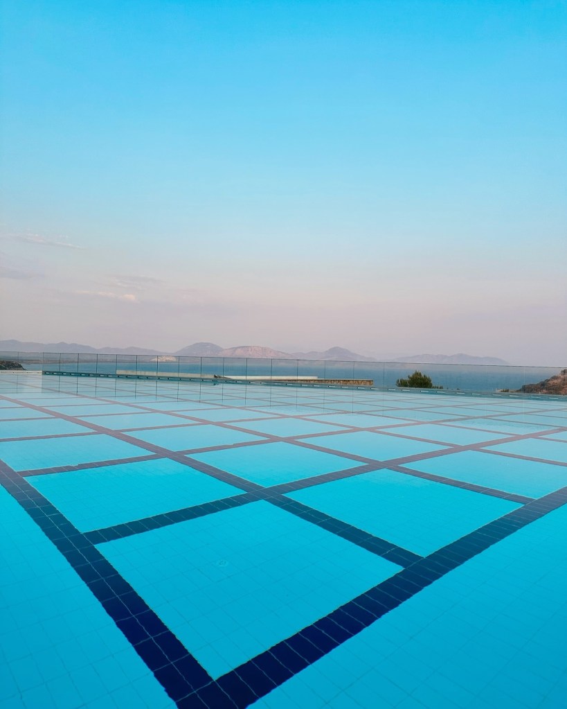 Infinity pool at TUI Blue Seno with panoramic views of the Mediterranean coastline, surrounded by lush greenery and sun loungers under parasols.
