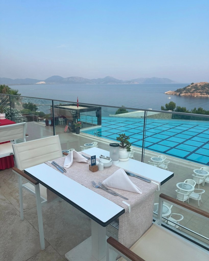 Infinity pool at TUI Blue Seno with panoramic views of the Mediterranean coastline, surrounded by lush greenery and sun loungers under parasols.