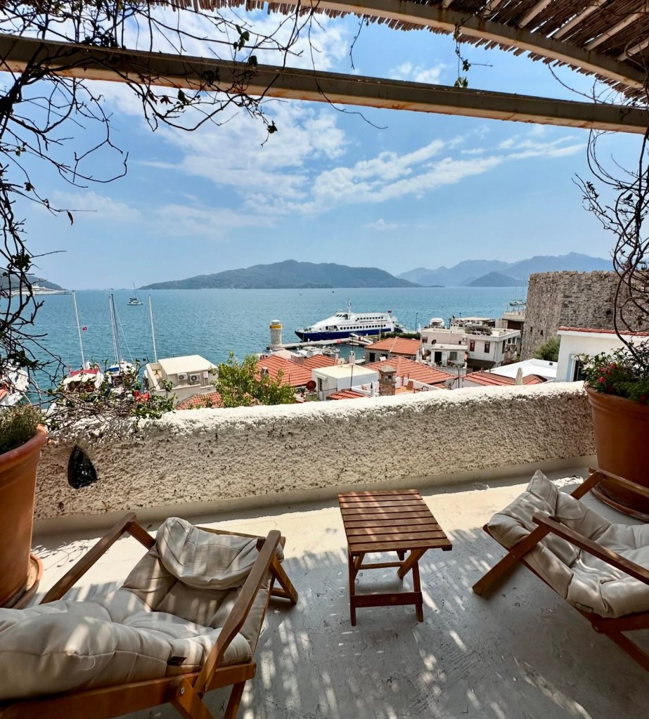 A breathtaking panoramic view of Marmaris, Türkiye, showcasing turquoise waters, lush green mountains, and a charming harbor filled with boats under a clear blue sky.