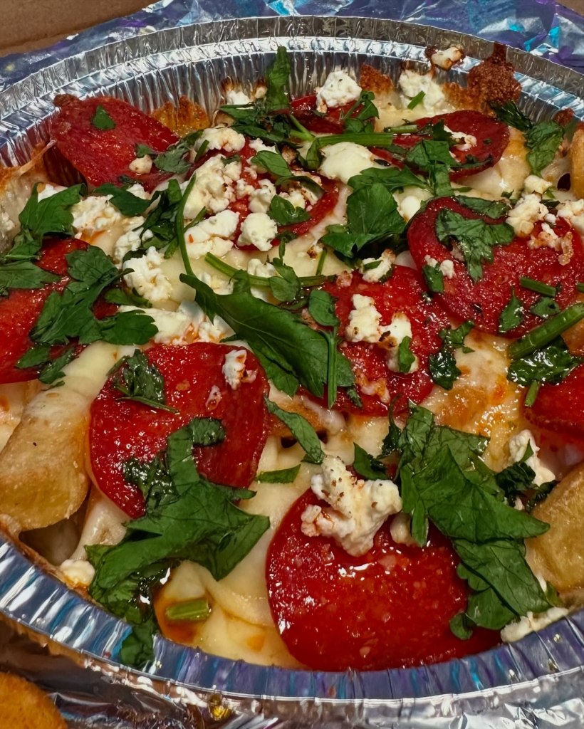 Hot honey-loaded chips topped with melting mozzarella, feta, pepperoni, and parsley, served in a takeaway box