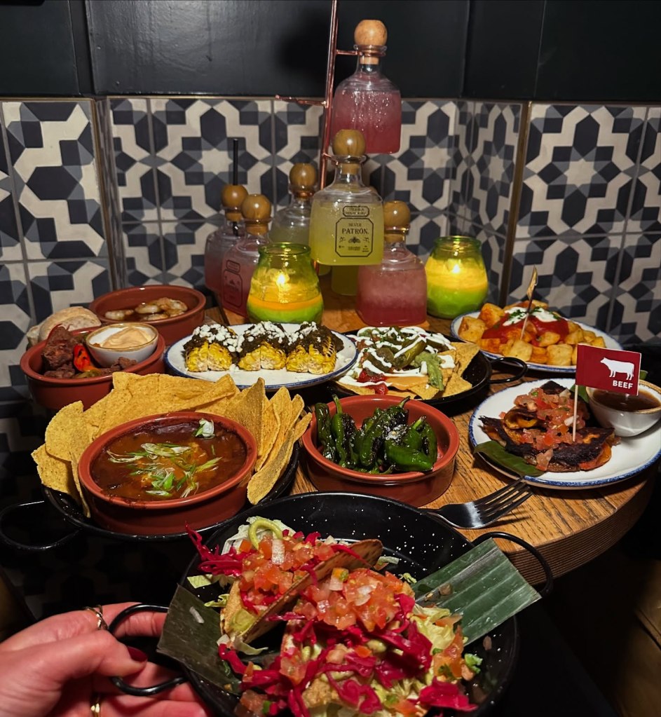 A vibrant table spread at a Cuban restaurant featuring a variety of tapas dishes and a margarita cocktail tree with colorful garnishes