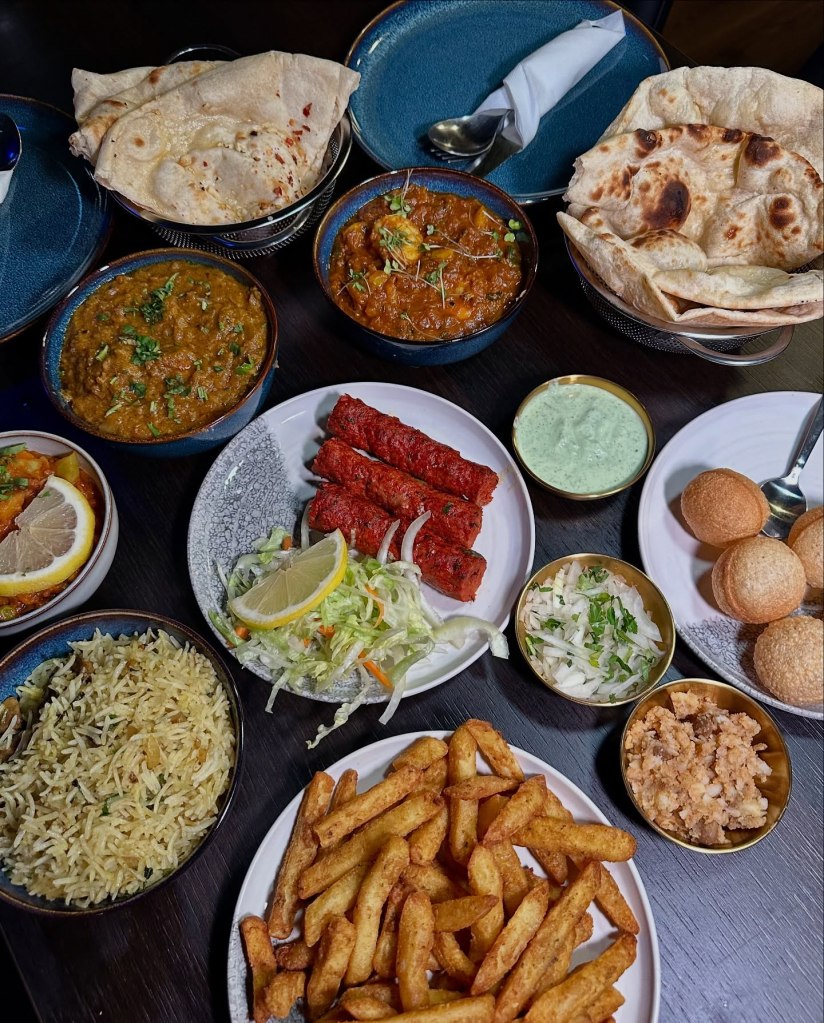 A beautifully arranged table at Sanskrit Restaurant in Newcastle, featuring a vibrant spread of Indian dishes including curries, naan breads, masala chips, mushroom rice, Pani Puri, and more