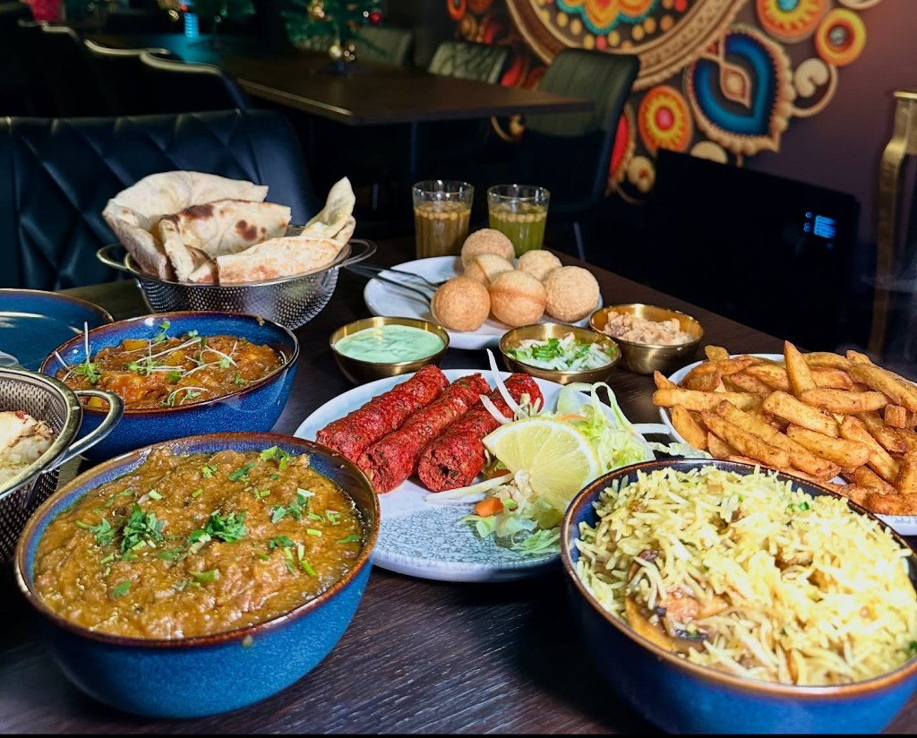 A beautifully arranged table at Sanskrit Restaurant in Newcastle, featuring a vibrant spread of Indian dishes including curries, naan breads, masala chips, mushroom rice, Pani Puri, and more