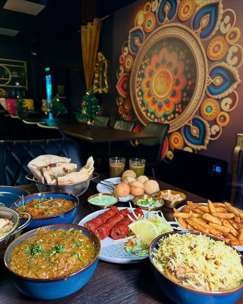 A beautifully arranged table at Sanskrit Restaurant in Newcastle, featuring a vibrant spread of Indian dishes including curries, naan breads, masala chips, mushroom rice, Pani Puri, and more