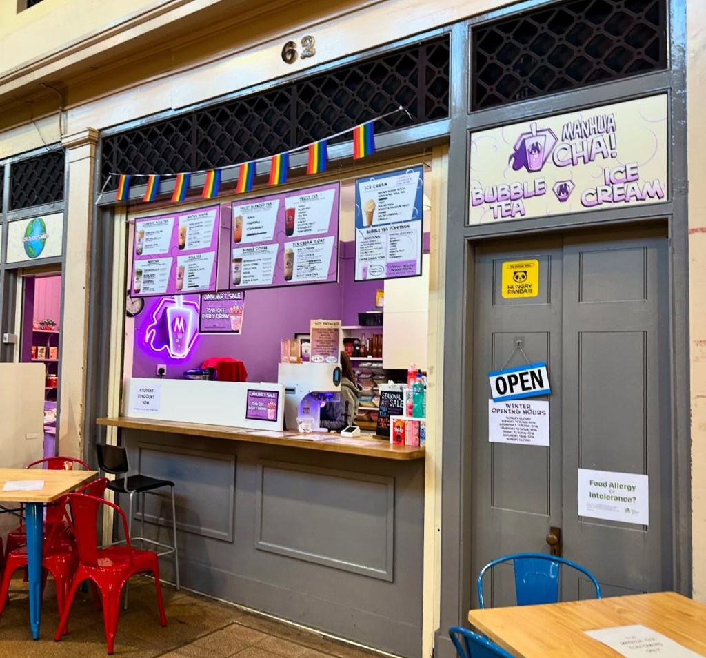 A cozy stall in the Grainger Market with bright signage, neatly stacked jars of sweets, and a modern bubble tea preparation area.