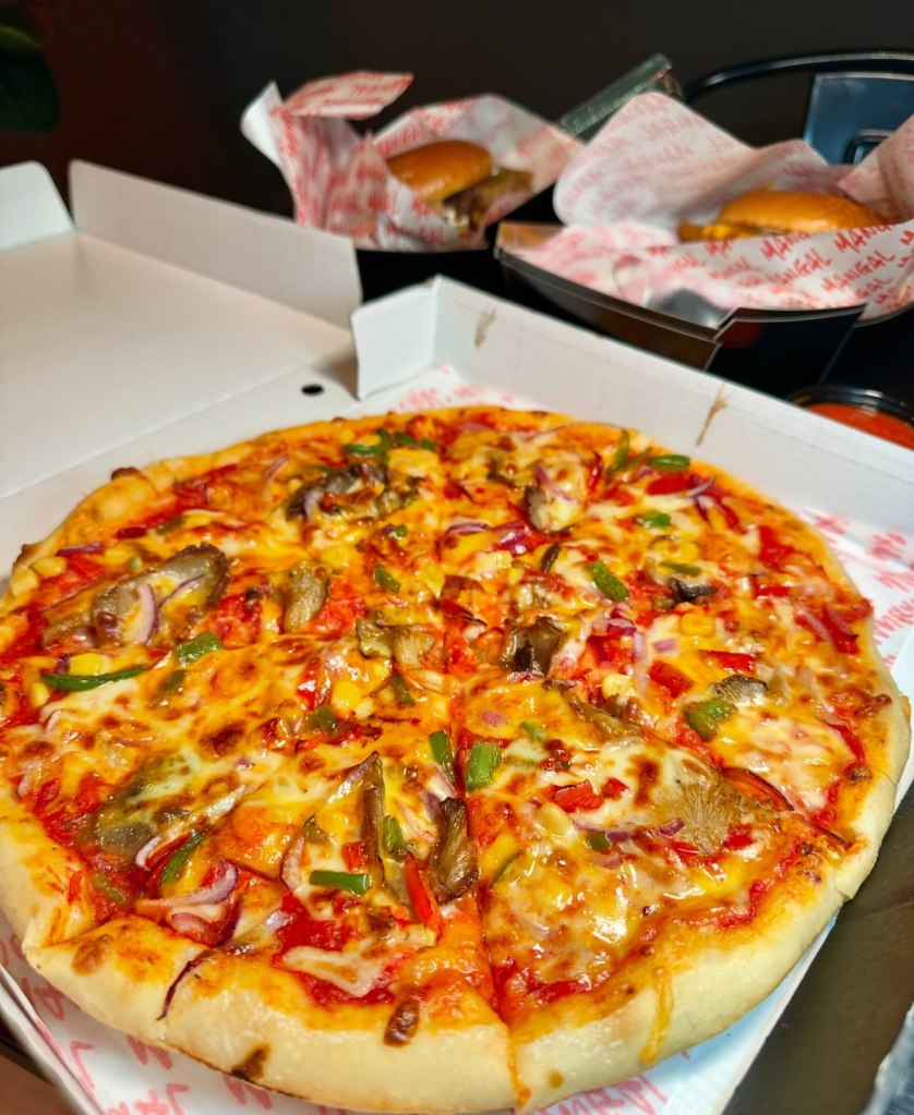 A freshly baked pizza topped with grilled oyster mushrooms, sweet corn, peppers, onions, and gooey melted cheese on a tangy tomato base.