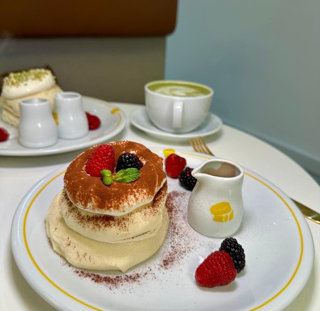 Tiramisu-flavored soufflé pancakes with creamy topping and cocoa powder dusting, served on a dessert plate.