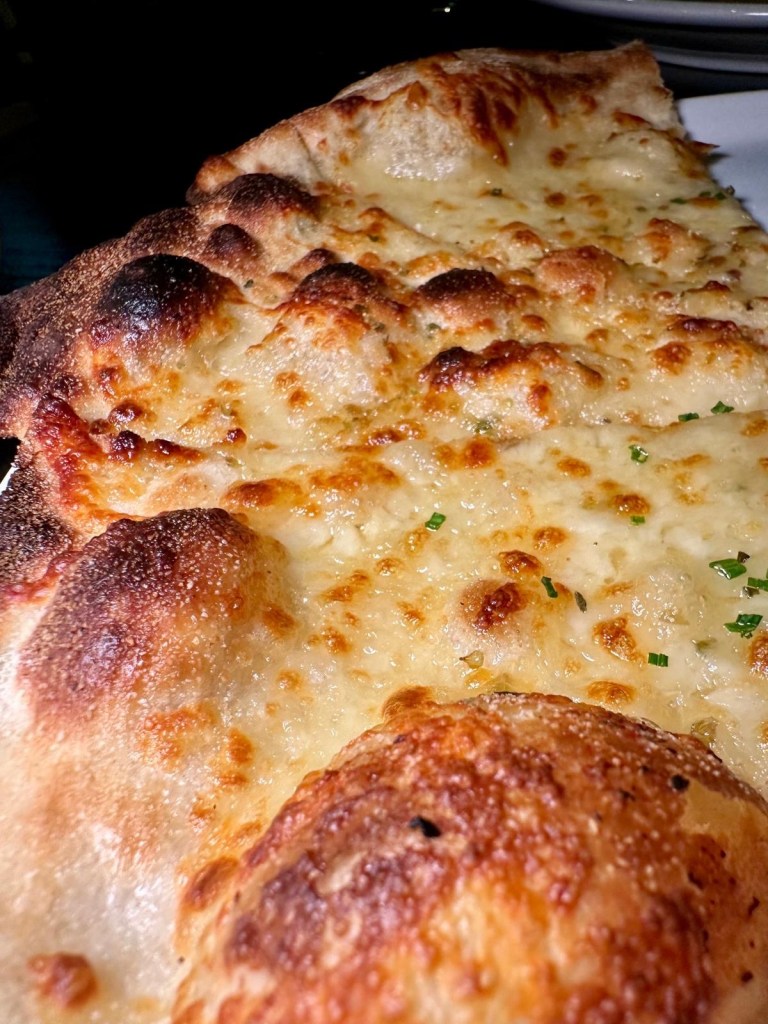 A thin, crispy garlic bread with a golden finish, garnished with herbs